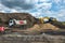 An excavator digs the ground and loads it into a dump truck outside the city. Road work on an intercity highway on a cloudy day