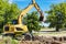 An excavator digs a pond pit in the garden against the blue sky. Digging a pit with an excavator. Earthmoving equipment and