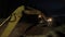 Excavator digs a trench with headlights at night. Work at night. Night shift construction. Mode of work and rest, safety