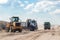 An excavator and dump trucks at the construction site outside the city. Road works on an intercity highway on a cloudy day