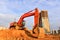 Excavator during excavation at construction site on sunset background. Red Backhoe on road work. Heavy Construction Equipment for