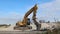 An excavator in front of a pile of  rubble  during an urban redevelopment. In the background two telescopic cranes