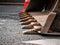 Excavator with hydraulic bucket stands on asphalt surface carriageway. Steel bucket tines close-up. Heavy powerful construction