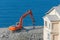 Excavator with hydraulic shears against the background of a demolished building. Dismantling of emergency construction standing on