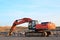 Excavator with a large iron bucket breaks asphalt on a construction site.