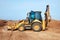 Excavator loader working at ground area on blue sky background, digging process. Yellow bucket.