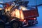 An excavator loads snow into the back of a dump truck at night.