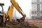 Excavator making trench on a building site with city on background