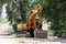 Excavator parked in shade of large trees waiting for trucks to load at large construction site