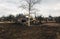 Excavator uprooting trees on land in countryside. Bulldozer clearing land from old trees, roots and branches with dirt and trash.