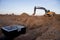 Excavator working at construction site on earthworks. Backhoe digs ground in pit for laying concrete sewer wells and sewage pipes