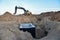 Excavator working at construction site on earthworks. Backhoe digs ground in pit for laying concrete sewer wells and sewage pipes