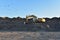 Excavator working at open pit mining. Backhoe digs gravel in sand quarry on blue sky background. Recycling old asphalt at a