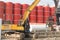 Excavator working beside red drilling solution tanks at construction site of subway station in Bangkok