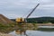 Excavator working in the river gravel quarry against the background of the forest. Extraction of natural resources