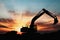 Excavators are digging the soil in the construction site on the sunset background.