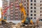 Excavators with raised buckets on the background of a multi-story residential building under construction