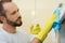 Excellent cleaning. Portrait of professional male cleaner wearing gloves, using spray detergent while cleaning kitchen