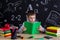 Excellent schoolboy sitting at the desk reading the book, surrounded with school supplies. Chalkboard as a background