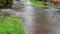 Excess rainwater flooding over an asphalt and gravel path with a grass lawn on both sides, public park and recreation area