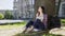 Exchange student sitting under tree, holding notebook, thinking on project