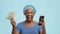 Excited African American Lady Holding Cellphone And Money, Blue Background