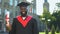 Excited afro-american student in graduation gown holding diploma looking camera