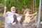 Excited amazed grandson child and grandfather swinging in summer garden. Granddad and grandchild sitting on swing in