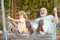 Excited amazed grandson child and grandfather swinging in summer garden. Granddad and grandchild sitting on swing in