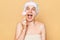 Excited amazed surpised woman wearing shower cap standing  over beige background making facial skin peeling with brush