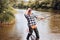 Excited angler senior man fisherman in cowboy hat with fishing rod, spinning reel on river. Old man catching fish