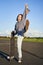 Excited asian girl dancing, standing with skateboard, skating on longboard and shouting carefree