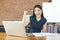 Excited Asian woman raising her arms while working on her laptop - success and business concept.