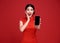 Excited Asian woman wearing traditional cheongsam qipao dress showing mobile phone isolated on red background