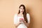 Excited birthday girl looking amazed, holding cake with candle, making b-day wish, standing on beige background