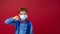 Excited boy in mask, glasses, with school backpack shows gesture of disapproval