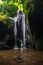 Excited Caucasian woman raising arms in front of the waterfall. Travel concept. View from back. Krisik waterfall. Bangli, Bali,