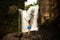 Excited Caucasian woman raising arms in front of waterfall. Travel concept. View from back. Tegenungan waterfall. Ubud, Bali,