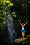 Excited Caucasian woman raising arms in front of waterfall. View from back. Near Tegenungan waterfall. Ubud, Bali, Indonesia