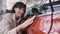 Excited Caucasian woman touching brand new red car in dealership smiling. Portrait of happy rich female client choosing