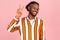 Excited cheerful afro-american man with beard and dreadlocks in eyeglasses and stylish striped shirt showing peace sign, v gesture