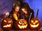 Excited children in Halloween costumes looking inside glowing jack o lantern in dark decorated room