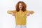Excited, curious redhead female with curly hair, wear yellow sweater, pointing down and looking amazed, pleasantly