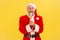 Excited elderly man with gray beard wearing santa claus costume holding and biting multicolored ice