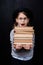 Excited elementary schoolgirl in hat and eyeglasses carrying stack of books