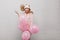 Excited fair-haired girl in pink pajamas holding bunch of helium balloons. Indoor portrait of inspired young lady in