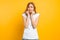 The excited girl is frightened by something, bites her nails, has a restless facial expression, stands on a yellow background