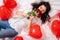 Excited Girl lying on bed red heart shape balloons with bouquet of flowers Woman rejoices gift on valentines day. Easy