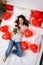 Excited Girl lying on bed red heart shape balloons with bouquet of flowers Woman rejoices gift on valentines day. Easy