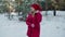 Excited girl in red coat and hat dancing in snowy woodland at winter walk. Laughing young woman dancing in winter forest